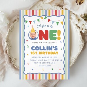 May include: A rectangular birthday invitation card with a vertical striped border in pink, yellow, blue, and green. The text reads It's fun to be ONE! Collin's 1st Birthday, Saturday, August 20, 2026, Collin's house, Any City, ST 12345, RSVP to Collin's mom 123-456-7890.