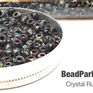 May include: A close-up of a small container filled with black, white, and red glass beads. The beads have a marbled or swirled pattern. The label on the container reads "BeadParlorBeads Crystal Ruby Picasso 4504 - 8 oz $5.70".