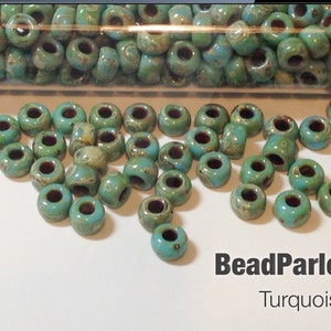 May include: Turquoise Picasso seed beads in a clear glass tube. The beads are a light turquoise color with brown and white speckles. The text "BeadParlorBeads Turquoise Picasso" is visible in the image.