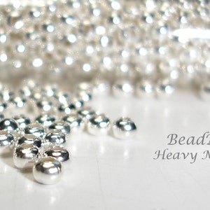 May include: A close-up of a pile of silver metal seed beads. The beads are small and round, and they have a shiny finish. The text "BeadParlorBeads Heavy Metal Seed Beads Silver" is visible in the image.