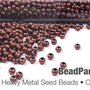 May include: Copper oxide heavy metal seed beads scattered on a white surface. The beads are a rich, metallic brown color and have a small hole through the center. The image includes the text "Bead Parlor Beads" and "Heavy Metal Seed Beads • Copper Oxide".