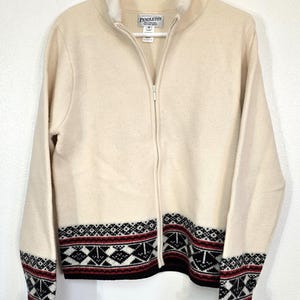 May include: Cream-colored zip-up sweater with a faux fur collar and cuffs. The sweater features a geometric pattern in black, red, and white along the bottom and cuffs. The brand name "Pendleton" is visible on a tag near the collar.