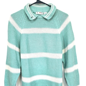 May include: A light blue and white striped sweater with a collared neckline. The sweater has long sleeves and a ribbed hem and cuffs. The collar is white with a small red and black logo.