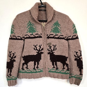 May include: A tan knitted zip-up sweater with a shawl collar. The sweater features a pattern of dark brown deer, green trees, and a dark brown border. The zipper is gold-colored.