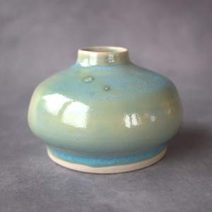 May include: A ceramic vase with a rounded body and a narrow neck. The vase has a gradient of colours, shifting from light green at the base to soft blue at the top. The base is white. A decorative piece for the home, ideal for displaying flowers or as a standalone ornament.