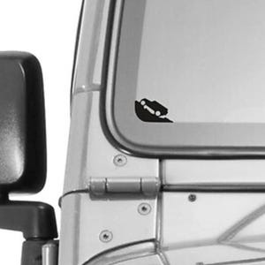 May include: A black vinyl decal of a vehicle climbing a steep incline is affixed to a vehicle window. The decal is a silhouette, showing the vehicle's body and wheels. The vehicle is angled upwards, suggesting off-road activity.