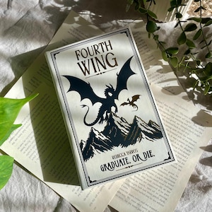 Peut inclure: Un livre relié intitulé Fourth Wing de Rebecca Yarros avec une couverture blanche présentant une illustration noire d'un dragon perché sur des sommets montagneux, un plus petit dragon en vol et le texte Graduate. Or Die. imprimé en noir.