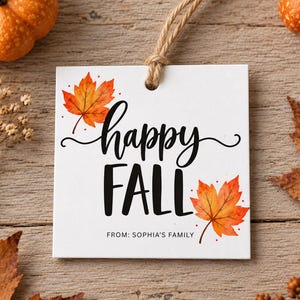 May include: A square white gift tag with a jute twine loop featuring watercolor orange and red maple leaves. The text reads "happy FALL" in black script and print, with "FROM: SOPHIA'S FAMILY" printed in smaller black capital letters below.