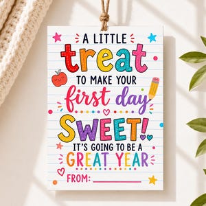 May include: A rectangular hanging sign with a white lined paper background featuring colorful text that reads: A LITTLE treat TO MAKE YOUR first day SWEET! IT'S GOING TO BE A GREAT YEAR FROM: with illustrations of a red apple, a pencil, and stars.
