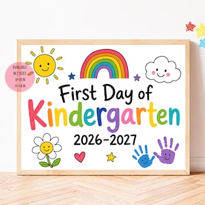 May include: A rectangular sign in a light wood frame featuring the text First Day of Kindergarten 2026-2027. The design includes a yellow sun, a rainbow, a white cloud, a flower, a pink heart, stars, and two handprints in blue and purple.