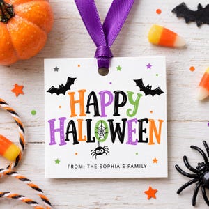 Puede incluir: Una etiqueta de regalo cuadrada blanca con una cinta morada, que presenta el texto "HAPPY HALLOWEEN" en letras coloridas, una telaraña, una araña y dos murciélagos negros. Debajo, la etiqueta dice "FROM: THE SOPHIA'S FAMILY" en fuente negra.