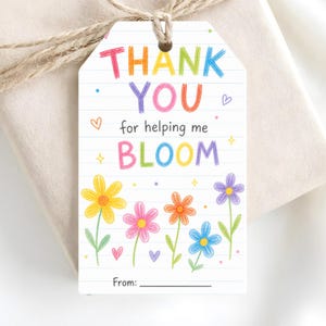 May include: A white gift tag with the words "THANK YOU" in rainbow colours, along with "for helping me BLOOM." The tag features colourful flowers and hearts. A twine string is attached.