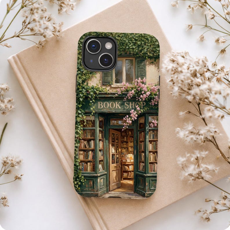 K&ouml;nnte beinhalten: Eine rechteckige Handyh&uuml;lle mit einer aufgedruckten Illustration einer Buchhandlung mit gr&uuml;nen Rahmen, Efeu und rosa Blumen. Der Eingang ist ge&ouml;ffnet und gibt den Blick auf Regale voller B&uuml;cher sowie den Schriftzug BOOK SHOP frei.