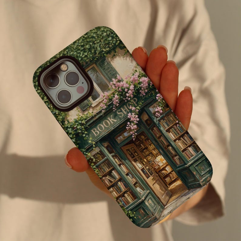 K&ouml;nnte beinhalten: Eine Smartphone-H&uuml;lle mit einer detaillierten Illustration einer Buchhandlung mit gr&uuml;nen Verzierungen, &uuml;ppigen rosa Blumen und Regalen voller B&uuml;cher, die durch die Glasfenster sichtbar sind. Der Text BOOK SHOP ist &uuml;ber der T&uuml;r aufgedruckt.
