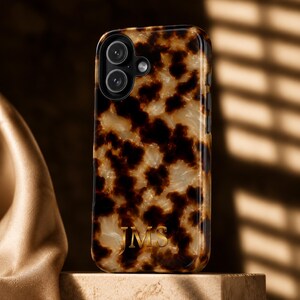 May include: A smartphone case featuring a glossy tortoiseshell pattern in shades of dark brown, amber, and cream. The case has a black camera cutout and the gold-colored letters JMS are printed in a serif font near the bottom center of the back.