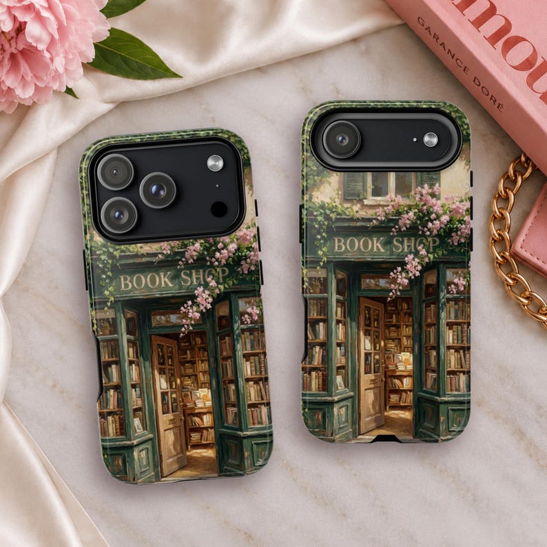 K&ouml;nnte beinhalten: Zwei Handyh&uuml;llen mit einer aufgedruckten Illustration eines gr&uuml;nen Ladenlokals mit dem Schriftzug BOOK SHOP &uuml;ber dem Eingang. Das Design zeigt mit B&uuml;chern gef&uuml;llte Regale, eine offene Holzt&uuml;r und rosa Blumen an der Fassade.