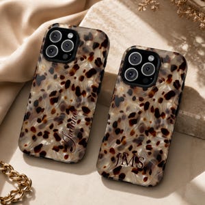 May include: Two rectangular smartphone cases featuring a glossy tortoiseshell pattern in shades of brown, black, and cream. One case is personalized with the script name Joanna, while the other features the block-letter monogram JMS in dark ink.