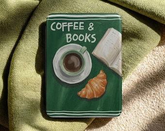 May include: A green book-shaped item with the words "COFFEE & BOOKS" in white. The cover features a coffee cup, saucer, open book, and croissant illustration. White border lines the edges of the book.