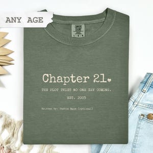 Puede incluir: Camiseta verde salvia con el texto "Chapter 21." y la frase "The plot twist no one saw coming." La camiseta también incluye el texto "EST. 2005" y "Written by: Custom Name (optional)." Una etiqueta dice "ANY AGE."