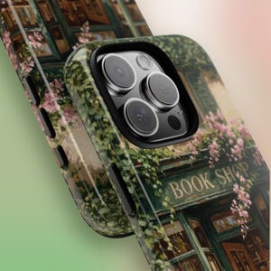 K&ouml;nnte beinhalten: Eine Smartphone-H&uuml;lle mit einem aufgedruckten Bild eines Ladenlokals und dem Schriftzug BOOK SHOP. Das Design zeigt gr&uuml;ne Kletterpflanzen und rosa Bl&uuml;ten an der Fassade. Die H&uuml;lle verf&uuml;gt &uuml;ber schwarze Seitentasten und einen Kameraausschnitt.