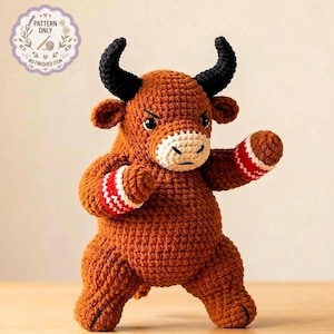 Puede incluir: Un toro marrón tejido a ganchillo con cuernos negros, hocico blanco y beige, y muñequeras a rayas rojas y blancas. El toro está en posición de combate. La imagen incluye un logotipo circular que dice "PATTERN ONLY" y "NO FINISHED ITEM".