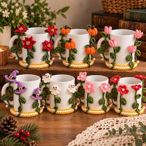 Puede incluir: Siete tazas de cerámica blanca decoradas con apliques de ganchillo. Los diseños incluyen flores de pascua rojas, calabazas naranjas, tulipanes rosas, sombreros de bruja morados, fantasmas blancos y flores rosas o rojas con tallos verdes.
