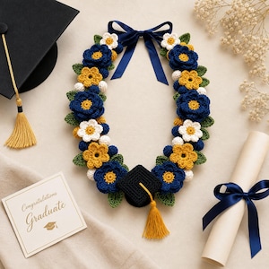 Peut inclure: Une guirlande de remise de diplôme faite à la main avec des fleurs au crochet bleues, jaunes et blanches, des feuilles vertes et un ruban bleu marine. Un petit chapeau de graduation noir avec un gland doré est attaché.