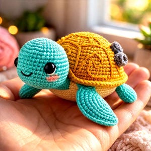 May include: A handmade crochet turtle in shades of teal, yellow, and beige. The turtle has a teal head with black eyes and a smiling face, a yellow shell, and teal flippers. A small gray bow is attached to the shell.