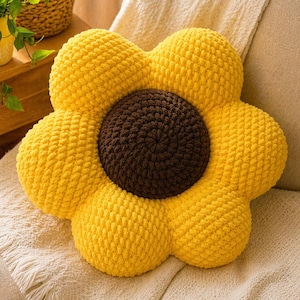May include: A flower-shaped throw pillow crafted from chunky, soft yellow yarn for the petals and dark brown yarn for the center. The pillow features a distinct, rounded petal design arranged in a circular pattern around a textured, spiral-stitched core.
