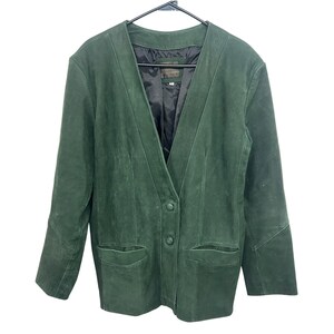 May include: A dark green suede blazer featuring a deep V-neckline, long sleeves, and two front buttons. The jacket includes two horizontal slit pockets at the waist and is lined with a smooth black interior fabric, hanging on a black hanger.