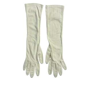 Può includere: Un paio di guanti lunghi da opera color bianco sporco realizzati in un tessuto liscio e opaco. Questi guanti superano il polso e presentano un sottile dettaglio di cucitura intrecciata o cordata che corre verticalmente lungo il bordo esterno di ogni braccio.