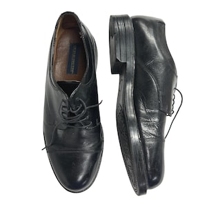 Peut inclure: Une paire de chaussures oxford en cuir noir avec un bout droit et des lacets noirs. L'intérieur de la chaussure présente une étiquette bleue avec le texte Giorgio Brutini. Les chaussures ont un talon empilé et une semelle en caoutchouc noir.