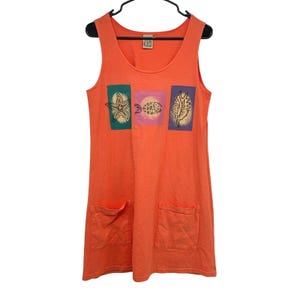 May include: A sleeveless orange tank dress featuring a scoop neckline and two front patch pockets. The chest area displays three rectangular graphic prints: a starfish on a teal background, a fish on a pink background, and a seashell on a purple background.