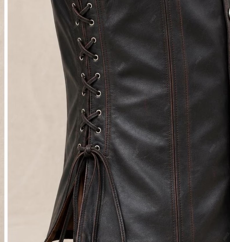 May include: A dark brown leather corset featuring vertical stitched panels and a side lacing system with silver-toned metal eyelets. The garment includes long, thin leather laces tied in a knot at the bottom, creating a structured fit.