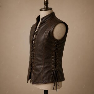 May include: A dark brown sleeveless vest featuring a high collar and a front lace-up closure with metal eyelets. The sides of the vest also include lace-up detailing with matching brown cords that tie at the bottom, creating a structured fit.