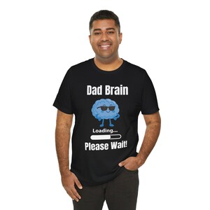 May include: A black short-sleeved t-shirt featuring a graphic of a light blue brain wearing black sunglasses. The text reads "Dad Brain" at the top, "Loading..." above a white progress bar, and "Please Wait!" at the bottom in white lettering.