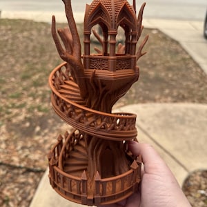 Könnte beinhalten: Ein braunes, 3D-gedrucktes Fantasy-Baumhaus mit einer Wendeltreppe und einer gazeboartigen Struktur an der Spitze. Das Baumhaus weist komplizierte Details auf und wird in einer Hand gehalten. Das Baumhaus ist ein einzigartiger Dekorationsartikel.