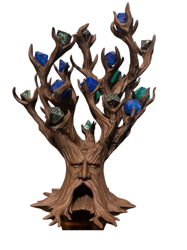 Puede incluir: Un soporte para dados en forma de &aacute;rbol marr&oacute;n, con una cara tallada en el tronco. Las ramas sostienen varios dados poli&eacute;dricos en tonos azules, verdes y plateados. La base es de color marr&oacute;n oscuro.