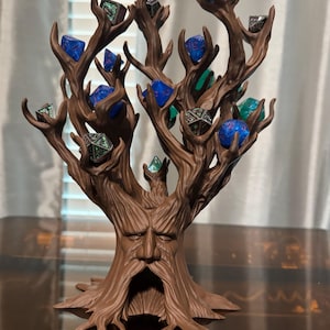Puede incluir: Un soporte para dados en forma de &aacute;rbol marr&oacute;n con una cara tallada en el tronco. Las ramas sostienen varios dados poli&eacute;dricos en tonos azules, verdes y plateados. Un accesorio &uacute;nico para juegos de mesa.