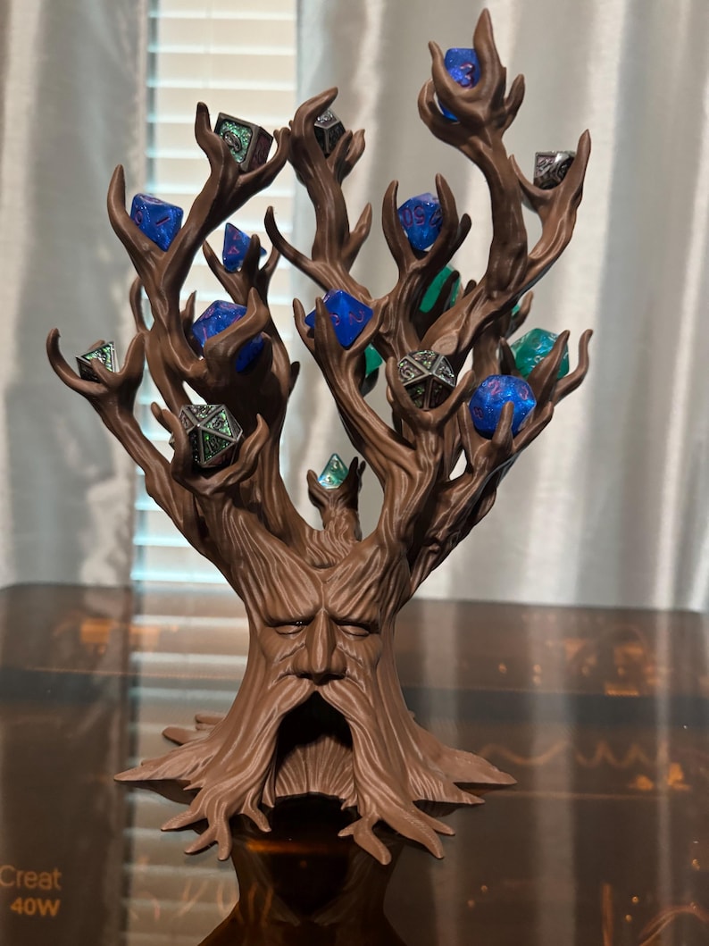 Puede incluir: Un soporte para dados en forma de &aacute;rbol marr&oacute;n con una cara tallada en el tronco. Las ramas sostienen varios dados poli&eacute;dricos en tonos azules, verdes y plateados. Un accesorio &uacute;nico para juegos de mesa.