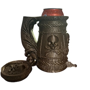 May include: A brown, pirate-themed mug with a skull and crossbones design. The mug has a handle and a lid attached by a hinge. A red can sits inside the mug. The mug is made of a textured material.