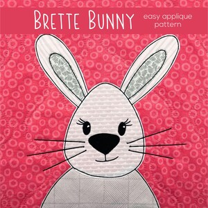 May include: A white bunny applique pattern with the text "Brette Bunny easy applique pattern". The bunny has a pink nose, black eyes, and a white and gray striped body. The background is a pink and white pattern of circles.