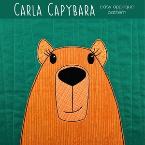 May include: An orange capybara applique pattern on a green background. The capybara has a black nose and eyes, with the text "CARLA CAPYBARA" at the top. The words "easy applique pattern" are also visible.
