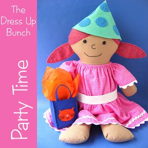 May include: A handmade doll wearing a pink dress with white polka dots and a green party hat with blue polka dots. The doll is holding a blue gift bag with a cat face on it. The doll is sitting on a blue background. The text "The Dress Up Bunch Party Time" is visible on the left side of the image.