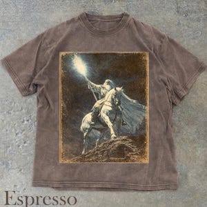 Puede incluir: Camiseta color espresso con una ilustraci&oacute;n vintage de un mago a caballo sosteniendo un bast&oacute;n brillante. El gr&aacute;fico tiene un borde desgastado. La camiseta tiene cuello redondo y mangas cortas.