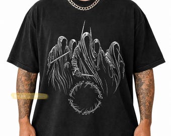 May include: A black short-sleeve t-shirt featuring a white graphic print of five hooded figures in robes holding blades. Below the figures is a circular ring design with intricate elvish-style script lettering. The shirt has a crew neckline.