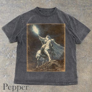 Pepper t-shirt featuring Gandalf on horseback with glowing staff in a vintage fantasy illustration, lord of the rings inspired wizard design, lotr fan art style graphic tee, magical wizard scene with detailed horse and mystical light, fantasy lover gift, wizard gift idea, lord of the ring shirt, gandalf shirt, fantasy aesthetic clothing, unisex streetwear tee, high quality print, perfect gift for lotr fans and magic lovers