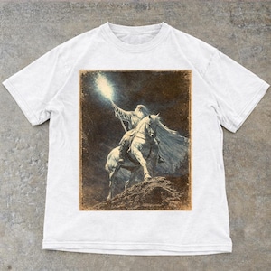 White Vintage Gandalf on horseback with glowing staff in a vintage fantasy illustration, lord of the rings inspired wizard design, lotr fan art style graphic tee, magical wizard scene with detailed horse and mystical light, fantasy lover gift, wizard gift idea, lord of the ring shirt, gandalf shirt, fantasy aesthetic clothing, unisex streetwear tee, high quality print, perfect gift for lotr fans and magic lovers