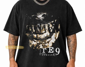 May include: A black short-sleeve t-shirt featuring a distressed graphic of a mouth with teeth in shades of white and gold. Below the graphic, the text reads rE9 and requiem in a white, weathered font. The shirt has a crew neckline.