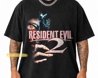 May include: Black graphic t-shirt featuring the Resident Evil 2 logo and a monster illustration. The design includes a close-up of a monster eye and hand. The shirt has a vintage, worn look.